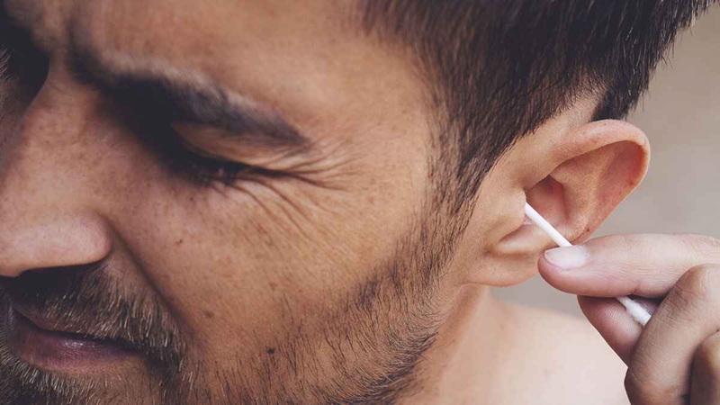 A man attempts to remove earwax with a q-tip. This is not advised, as you will typically only end up pushing the wax down, making the problem worse. It is also dangerous, and many people have accidentally damaged their eardrum or middle ear.