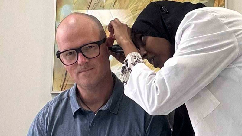Examination of the first author's ear with a hand-held otoscope by one of his students.